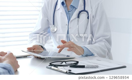 Female medical professional reviewing health information on digital tablet, explaining diagnosis to patient during clinical consultation. Medicine and healthcare concept Female medical professional reviewing health information on digital tablet, explaining diagnosis to patient during clinical consultation. Medicine and healthcare concept 129658934