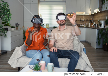 Multi-ethnic couple using vr headset in living room Multi-ethnic couple using vr headset in living room 129658935