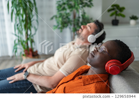 Two friends relaxing on the sofa listening to music with headphones 129658944