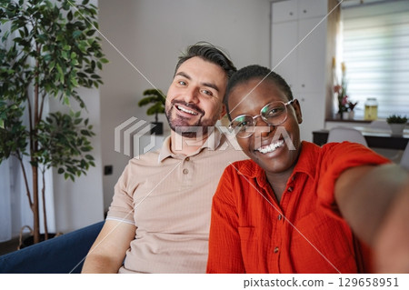 Happy multi-ethnic couple taking a selfie on the couch at home 129658951