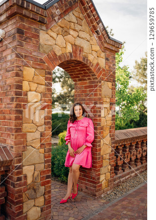 happy pregnant young woman in pink dress by the stone fence happy pregnant young woman in pink dress by the stone fence 129659785