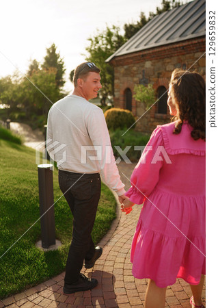 pregnant brunette woman in pink dress holding man's hand and following him. pregnant brunette woman in pink dress holding man's hand and following him. 129659832