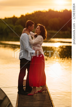 man and pregnant woman in red dress at sunset on the pier  129659864