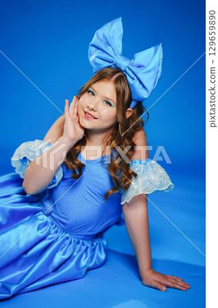 Cute teenage girl in blue doll dress with big blue bow posing lying on the floor Cute teenage girl in blue doll dress with big blue bow posing lying on the floor 129659890