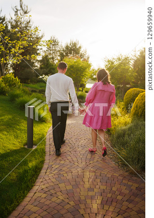 pregnant brunette woman in pink dress holding man's hand and following him. 129659940