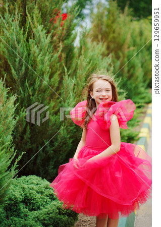 A girl in a lush pink dress near the green bushes A girl in a lush pink dress near the green bushes 129659951