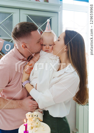 Mom and dad hold little daughter by the birthday cake. Mom and dad hold little daughter by the birthday cake. 129659968
