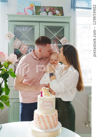 Mom and dad hold little daughter by the birthday cake.  129659982