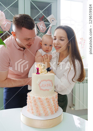 Mom and dad hold little daughter by the birthday cake.  129659984