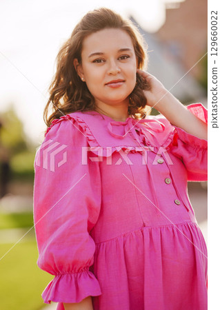 Beautiful and happy pregnant young woman in pink dress on a walk in the park 129660022