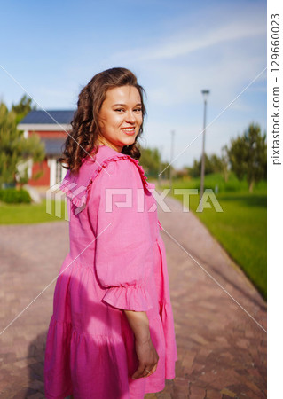 Beautiful pregnant young woman in pink dress on the path. view from the back 129660023