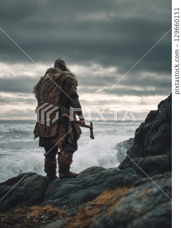 Rugged Viking warrior in fur and leather stands by crashing sea waves. Moody Nordic scene evokes strength, history, tradition, and ancient Norse legend 129660151