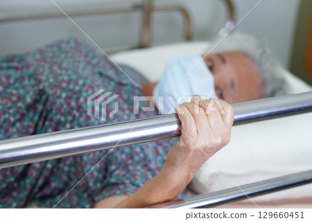 Asian elder senior woman patient holding bed rail while lie down with hope waiting her family in hospital. Asian elder senior woman patient holding bed rail while lie down with hope waiting her family in hospital. 129660451