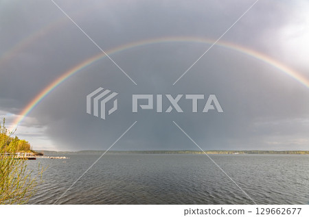 Rainbow over Blue lake with cloudy sky 129662677