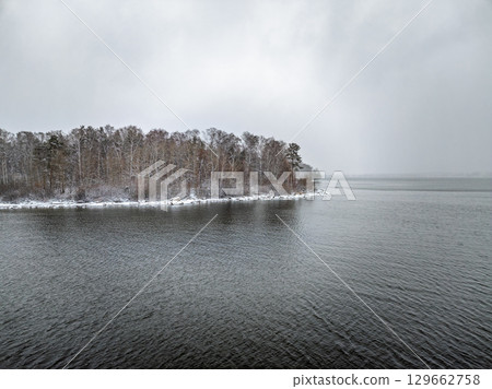 November landscape with covered with first snow birch and spruce forest on lake shore. First snow on lake. November landscape with covered with first snow birch and spruce forest on lake shore. First snow on lake. 129662758
