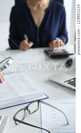 Two professional chartered accountants reviewing financial reports and analyzing data using a calculator and a magnifying glass, ensuring accuracy and compliance. Audit and taxes in business 129663224
