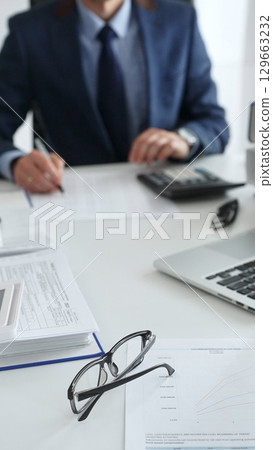 Close up of female accountant hands using calculator while collaborating with male colleague in office, calculating taxes and analyzing financial data. Audit and taxes in business Close up of female accountant hands using calculator while collaborating with male colleague in office, calculating taxes and analyzing financial data. Audit and taxes in business 129663232