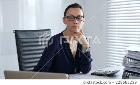 Businesswoman signing and reviewing accounting documents while calculating financial data in a corporate office setting. Audit and taxes in business Businesswoman signing and reviewing accounting documents while calculating financial data in a corporate office setting. Audit and taxes in business 129663259