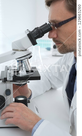 Medical scientist wearing glasses using microscope analyzing samples in modern laboratory doing scientific research. Medicine, health care and science concept Medical scientist wearing glasses using microscope analyzing samples in modern laboratory doing scientific research. Medicine, health care and science concept 129663260