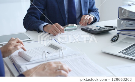 Business team analyzing financial documents, using calculators and laptop, working together on project in modern office. Audit and taxes concept 129663263