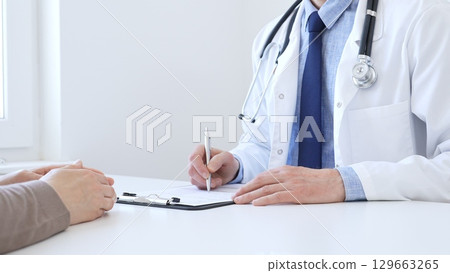 Doctor man taking notes while listening to a female patient explaining her symptoms during a medical consultation in the clinic office. Medicine and health care concept 129663265