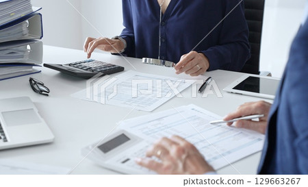 Business team of male and female accountants analyzing financial documents, using calculators and laptop, working together on project in modern office. Audit and taxes concept 129663267