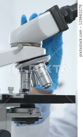 Close up of blue gloved scientist's hand adjusting microscope in modern laboratory setting. Medicine, science and health care concept Close up of blue gloved scientist's hand adjusting microscope in modern laboratory setting. Medicine, science and health care concept 129663278