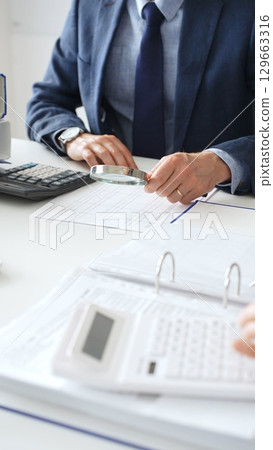 Business team analyzing financial documents, using calculators and laptop, working together on project in modern office. Audit and taxes concept 129663316