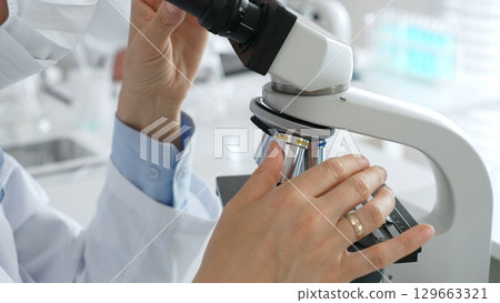 Gloved hands adjusting a microscope in a bright laboratory, emphasizing precision and focus in scientific research. Medicine, healthcare and science concept 129663321
