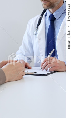 Unknown male doctor taking notes while listening to a female patient explaining her symptoms during a medical consultation in the clinic office. Medicine concept Unknown male doctor taking notes while listening to a female patient explaining her symptoms during a medical consultation in the clinic office. Medicine concept 129663333