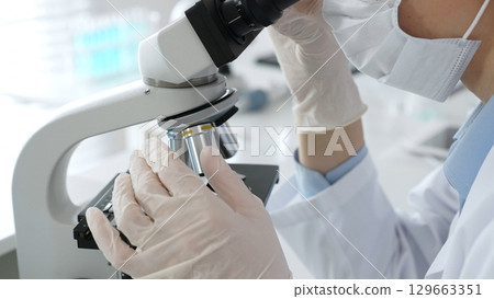 White gloved hands of scientist professional adjusting a microscope in a bright laboratory, emphasizing precision and focus in scientific research. Medicine, healthcare and science concept 129663351