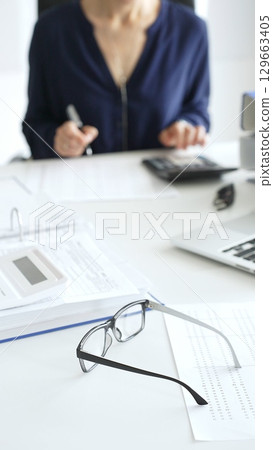 Professional analyzing financial data, writing notes near laptop, magnifying glass, documents, binders on workplace desk. Audit and taxes concept 129663405