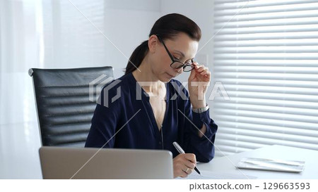 Businesswoman reviewing accounting documents while calculating financial data in modern office setting. Business people concept 129663593