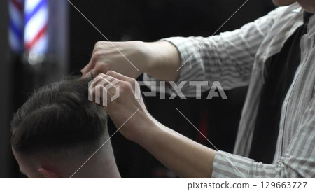 Professional barber carefully combing client's hair, preparing precise hairstyle with expert grooming techniques in modern barbershop setting 129663727