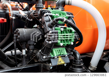 Close-up of industrial pump with green and black components, orange background. Close-up of industrial pump with green and black components, orange background. 129663861