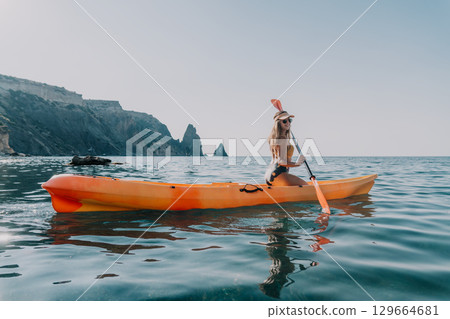 Kayaking Woman Sea Coastal Landscape - A woman enjoys kayaking in calm waters near a scenic coastline with rocky cliffs on a sunny day. Kayaking Woman Sea Coastal Landscape - A woman enjoys kayaking in calm waters near a scenic coastline with rocky cliffs on a sunny day. 129664681