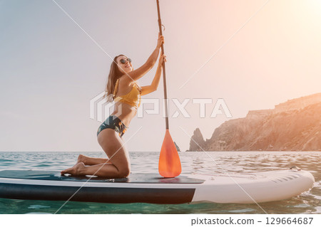 Woman Paddleboarding Ocean - Young woman enjoys paddleboarding on a calm ocean with a scenic background. 129664687