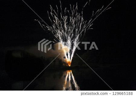 Celebration features colorful fireworks reflecting over calm lake during summer night Celebration features colorful fireworks reflecting over calm lake during summer night 129665188