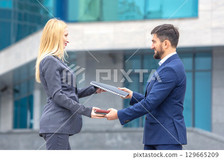 Business professionals exchanging documents outdoors in a modern urban setting during daytime 129665209