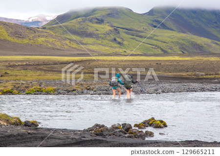 Exploring the rugged landscape of Iceland with hikers crossing a river on a cloudy day 129665211