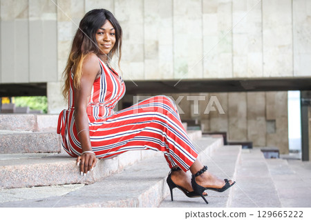 African woman sitting elegantly on steps in a stylish outfit during daytime African woman sitting elegantly on steps in a stylish outfit during daytime 129665222