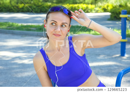 Young woman enjoys warm sunny day while listening to music in vibrant workout attire Young woman enjoys warm sunny day while listening to music in vibrant workout attire 129665223