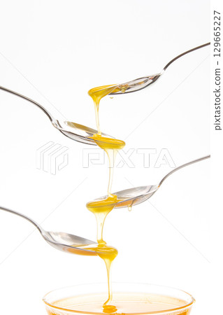 Honey drips from spoon to spoon in creative stacking arrangement indoors Honey drips from spoon to spoon in creative stacking arrangement indoors 129665227