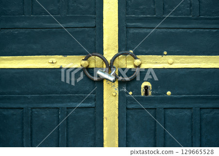 Blue Metal Door Secured with Padlock and Yellow Painted Cross 129665528