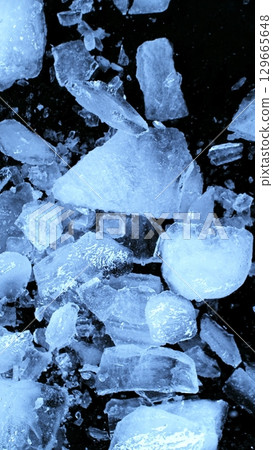 Broken Ice. Crushed Textured Ice with Cracks on a Black Background, Close-up. Abstract Background with Crushed Ice Pieces. Vertical Aspect Ratio. 129665648