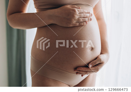 Close up of a cute pregnant belly. Pregnant woman holds hands on belly touching her baby caring about her health. Motherhood concept 129666473