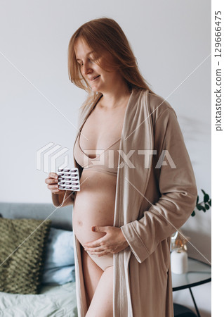 belly of pregnant woman and vitamin pills in the hand. Pregnant woman taking vitamins and minerals at home. Pregnant girl monitors their health. Medicine banner belly of pregnant woman and vitamin pills in the hand. Pregnant woman taking vitamins and minerals at home. Pregnant girl monitors their health. Medicine banner 129666475