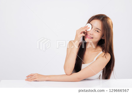 Pad glides softly as she presses a cotton pad to her face, removing makeup with ease and celebrating skincare and freshness. isolated studio white background Pad glides softly as she presses a cotton pad to her face, removing makeup with ease and celebrating skincare and freshness. isolated studio white background 129666567