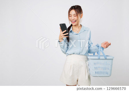 Grocery shopping Asian woman with basket holding phone and mobile app showing supermarket shopping lifestyle and happy online commerce habits. isolated studio white background Grocery shopping Asian woman with basket holding phone and mobile app showing supermarket shopping lifestyle and happy online commerce habits. isolated studio white background 129666570