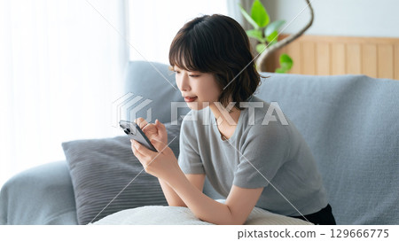 坐長沙發和使用智能手機的婦女 坐長沙發和使用智能手機的婦女 129666775